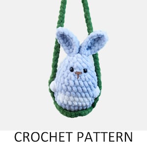May include: A crocheted blue bunny with white accents hanging from a green strap. The bunny has a brown nose and black eyes.  CROCHET PATTERN is written below the bunny.