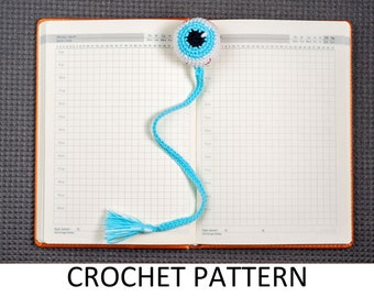 May include: A blue crocheted eye bookmark with a black pupil and white sclera. The bookmark is attached to a blue crocheted cord with a white tassel.