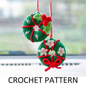 May include: Two crocheted Christmas wreaths with red ribbon and white flowers hanging from a rearview mirror. The wreaths are green and red with white accents.  CROCHET PATTERN is written below the image.