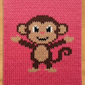 May include: A pink knitted square featuring a pixelated monkey design. The monkey has brown and tan fur, black eyes, and a small smile. The background is a solid, textured pink.