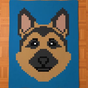 May include: A blue blanket featuring a pixelated image of a German Shepherd dog's face. The dog's face is brown, black, and tan, with a black nose and eyes. The blanket is rectangular and made of a soft material.