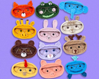 May include: Twelve crocheted animal-shaped eyeglass holders. Each holder features a different animal, including a fox, frog, elephant, llama, reindeer, bear, cat, pig, and a blue creature. The holders are all made with soft yarn and have a cute and whimsical design.