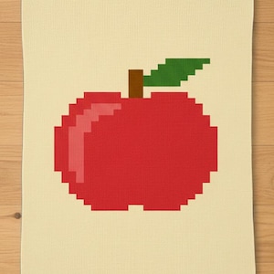May include: A cream-colored kitchen towel featuring a pixelated red apple design with a brown stem and green leaf. The apple is the focal point, rendered in a blocky, retro style, adding a touch of whimsy to the kitchen decor.