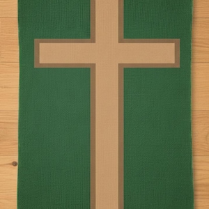 Puede incluir: Un textil rectangular verde con una gran cruz beige en el centro. La cruz tiene un borde beige más oscuro. El textil está colocado sobre una superficie de madera marrón claro.