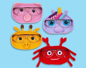 May include: Four crocheted animal-shaped eyeglass holders. A pink pig, a purple unicorn, a yellow giraffe, and a red crab. Each holder has a pair of clear glasses inside.