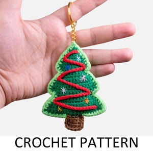 Peut inclure: Une décoration de Noël en forme de sapin de Noël crocheté en vert avec du fil rouge pour les lumières et du fil blanc pour les étoiles. L'ornement est attaché à un porte-clés doré.