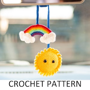 May include: A crocheted rainbow with white clouds and a yellow sun with a smiling face hanging from a rearview mirror.  The rainbow is made of red, orange, yellow, green, blue, indigo, and violet yarn.  The sun is made of yellow yarn and has black eyes.  The crocheted sun and rainbow are hanging from a blue string.