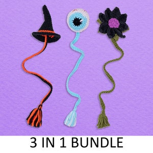 Op de afbeelding: Een set van drie Halloween-thema gehäkelde bladwijzers. Eén bladwijzer heeft een zwarte heksenhoed met een oranje en zwarte kwast, een andere heeft een blauw oog met een witte en blauwe kwast, en de laatste bladwijzer heeft een zwarte bloem met een paarse kern en een groene kwast. De tekst "3 IN 1 BUNDLE" is onder de bladwijzers afgedrukt.