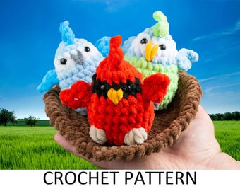 May include: Three crocheted birds in a brown crocheted nest. The birds are a red cardinal, a light blue bird, and a green and light blue bird.