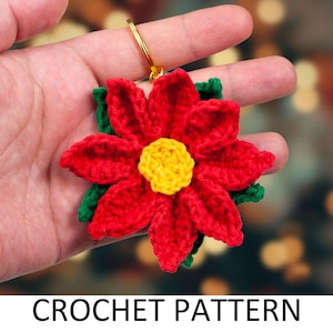 May include: Crochet pattern for a red poinsettia flower with a yellow centre and green leaves. The flower is attached to a gold key ring.