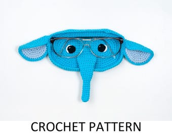 May include: A handmade, blue crochet elephant-shaped glasses case with gray accents on the ears. The case holds a pair of silver-framed glasses. The text "CROCHET PATTERN" is displayed at the bottom of the image.