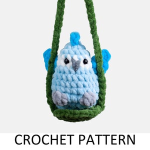 以下が含まれることがあります： 手編みの鳥のぬいぐるみ。水色の鳥が緑色のブランコに座っています。鳥はグレーと白のアクセントがあり、ブランコは緑色です。「CROCHET PATTERN」の文字が画像の下に表示されています。
