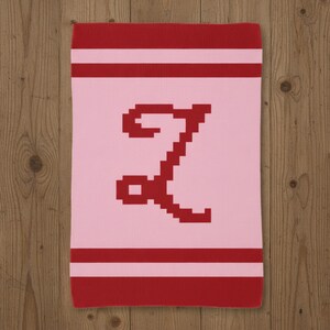 May include: A pink blanket with a red letter "Z" in the center. The blanket has red stripes at the top and bottom, and a red border. The letter "Z" is in a pixelated font.
