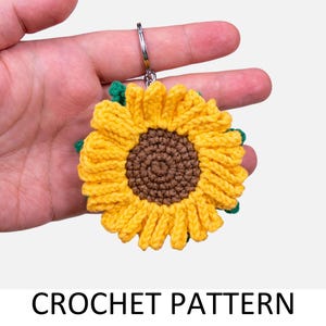 May include: A handmade crochet sunflower keychain with a yellow and brown design. The sunflower has yellow petals, a brown center, and green accents. The keychain is attached to a silver metal ring. The text "CROCHET PATTERN" is at the bottom.