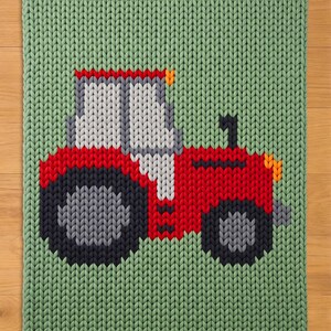May include: A knitted green blanket with a red tractor design. The tractor has grey and black wheels, a white and grey cab, and orange headlights. The blanket is made of a chunky knit material.