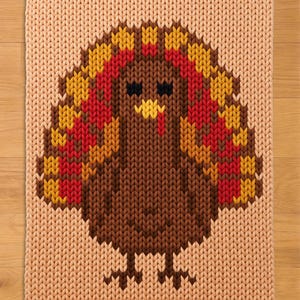 May include: A rectangular knit blanket featuring a central turkey graphic. The turkey is rendered in shades of brown, yellow, red, and orange against a light peach background. The knit texture is visible throughout the entire piece.