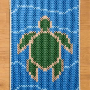 May include: A knitted square rug featuring a green turtle swimming in blue water. The turtle is outlined in a light tan color, and the water has white wave patterns. The rug has a white border.
