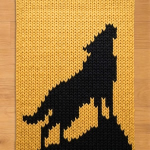 May include: A rectangular, knitted rug featuring a black silhouette of a howling wolf against a yellow background. The rug has a thick, textured appearance, with the wolf design prominently displayed. The rug is suitable for home decor.