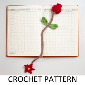 Peut inclure: Un marque-page en crochet en forme de fleur avec une fleur rouge et des feuilles vertes. Le marque-page est attaché à un carnet avec un motif quadrillé.