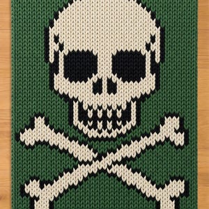 Puede incluir: Un tejido rectangular de punto con un diseño prominente de calavera y huesos cruzados. El fondo es de color verde bosque profundo, mientras que la calavera y los huesos están hechos de hilo color crema con detalles en negro para las cuencas y dientes.