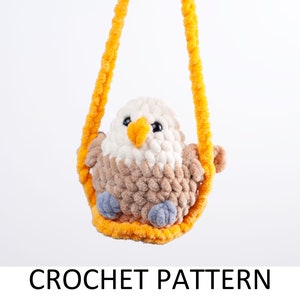 Può includere: Un giocattolo amigurumi a forma di aquila all'uncinetto appeso a un'altalena di filo giallo. L'aquila ha dettagli in filo marrone, bianco e blu.