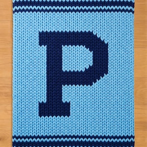 May include: A knitted blanket in light blue with a large navy blue letter "P" in the centre. The blanket has navy blue stripes at the top and bottom. The blanket is made of a chunky knit material.