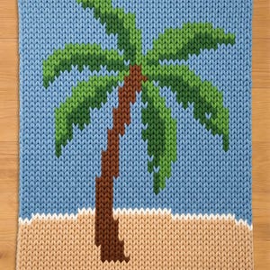Könnte beinhalten: Gestricktes Quadrat mit einem pixeligen Palmen-Design. Der Baum hat einen braunen Stamm und grüne Wedel vor einem hellblauen Himmel. Der untere Teil des Quadrats hat einen beigen Abschnitt, der Sand darstellt.
