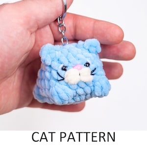 May include: A light blue crocheted cat keychain with black eyes, a white nose, and pink whiskers.  The keychain is attached to a silver metal ring.