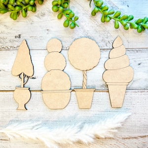May include: Four wooden cutouts of different trees and a potted plant. The cutouts are in the shape of a topiary, a tree with a single trunk, a tree with multiple trunks, and a potted plant. The cutouts are all brown and have a natural wood finish.