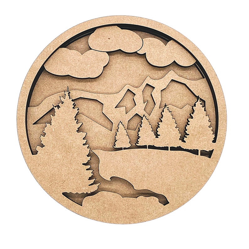 May include: A round wooden wall decor with a cutout design of a mountain landscape with trees and clouds. The wood is a light brown color.