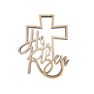 May include: Wooden cross-shaped decoration with the words "He is Risen" in a cursive font. The cross and text are cut from light-colored wood, creating a layered effect. Perfect for Easter or religious decor.