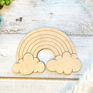 Op de afbeelding: Een houten regenboog uitsnijding met wolken aan beide kanten. De regenboog heeft vijf bogen en de wolken zijn eenvoudig en afgerond.