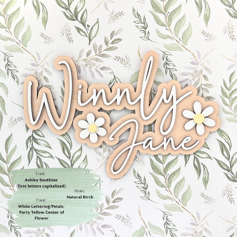 May include: A wooden wall sign featuring the name Winnly Jane in white script lettering layered over a natural birch wood backing. Two white daisies with yellow centers are attached to the sign. Text on the image specifies font, stain, and paint.