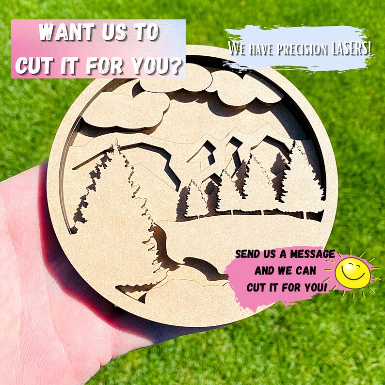 May include: A wooden round cutout of a mountain scene with trees and a sky. The text "WANT US TO CUT IT FOR YOU?" is at the top of the image. The text "WE HAVE PRECISION LASERS!" is at the top right of the image. The text "SEND US A MESSAGE AND WE CAN CUT IT FOR YOU!" is at the bottom of the image.