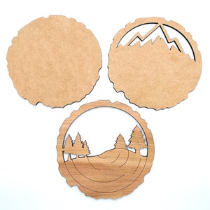 May include: Three wooden coasters with different designs. One coaster features a mountain range, another has a forest scene, and the third is plain.