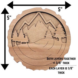 May include: A wooden wall art piece with a mountain and forest scene. The art is 5 inches in diameter and 3/8 inch thick. It is made of two layers of wood, each 1/8 inch thick.