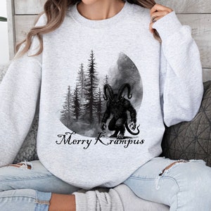 May include: A gray sweatshirt with a black and white illustration of a monster with horns and a forest scene. The text "Merry Krampus" is printed below the illustration.
