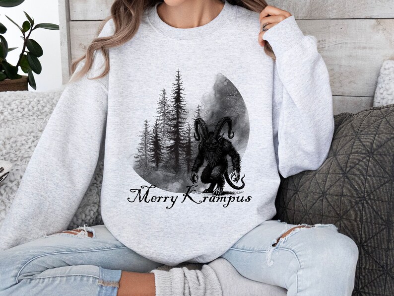 May include: A gray sweatshirt with a black and white illustration of a monster with horns and a forest scene. The text "Merry Krampus" is printed below the illustration.