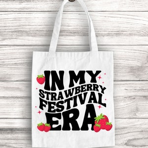 May include: White tote bag with black text that reads "In My Strawberry Festival Era" with red strawberry illustrations.
