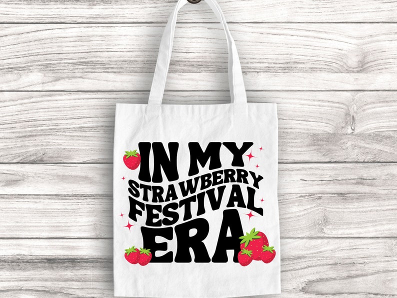 May include: White tote bag with black text that reads "In My Strawberry Festival Era" with red strawberry illustrations.