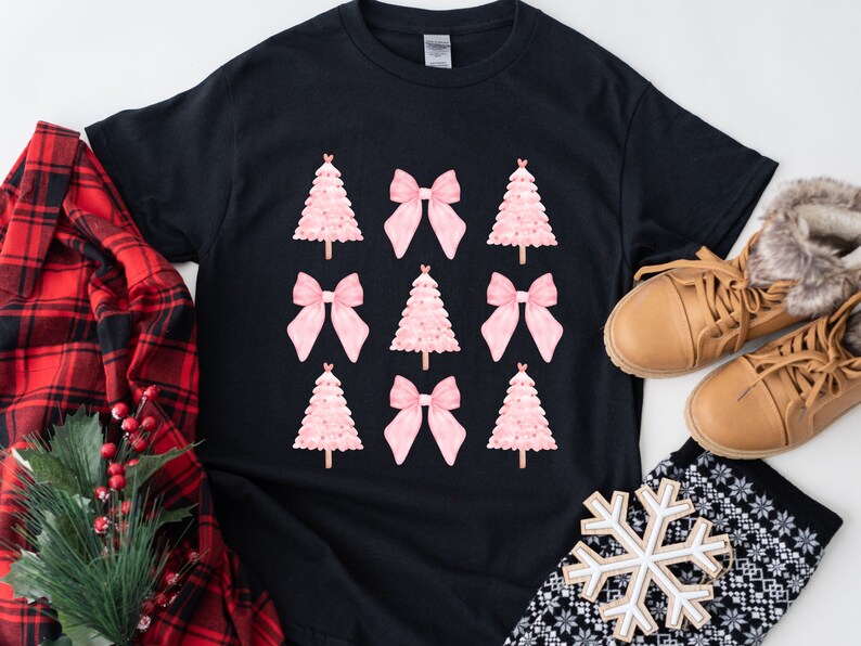 May include: Black t-shirt featuring a pattern of pink Christmas trees and bows. The shirt is surrounded by a red plaid shirt, brown boots, and a snowflake ornament, suggesting a holiday theme.