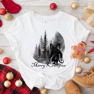 May include: White t-shirt with a black and white illustration of a monster with horns and a forest in the background. The text "Merry Krampus" is printed below the illustration.