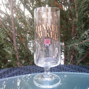 May include: A clear glass beer stein with a gold logo that says "Denkelf Acker" and a red and white logo with the letters "CD".