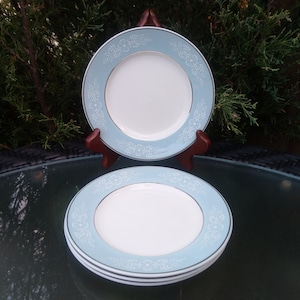 May include: Three blue and white ceramic dinner plates with a delicate floral pattern. The plates are stacked on a wooden stand.