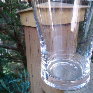 May include: A clear glass drinking glass with a wide base and a rounded top. The glass is sitting on a wooden surface.