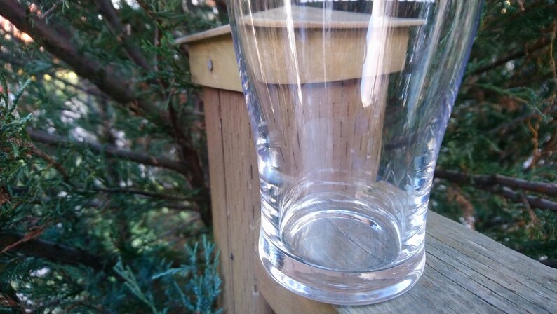 May include: A clear glass drinking glass with a wide base and a rounded top. The glass is sitting on a wooden surface.