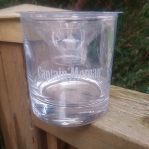 Puede incluir: Un vaso transparente con las palabras "Captain Morgan" grabadas en el lateral. El vaso está sobre una superficie de madera.