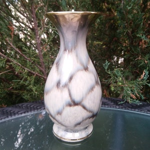 May include: A white ceramic vase with a brown and gray marbled pattern. The vase has a gold rim and a gold base.