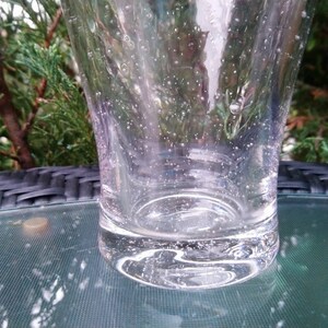 May include: A clear glass tumbler with a textured surface and small air bubbles throughout. The glass is sitting on a black and green surface.