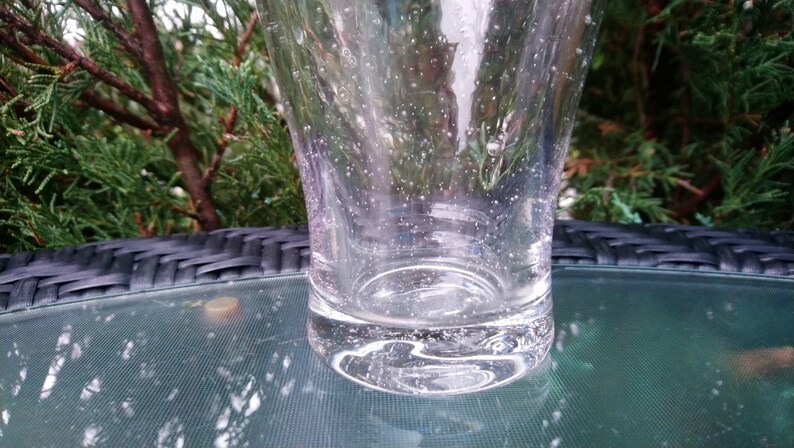 May include: A clear glass tumbler with a textured surface and small air bubbles throughout. The glass is sitting on a black and green surface.